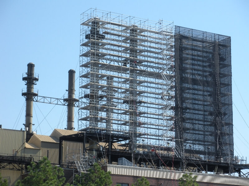 An elaborate and impressive industrial scaffolding setup is seen towering above the smoke stacks of a factory